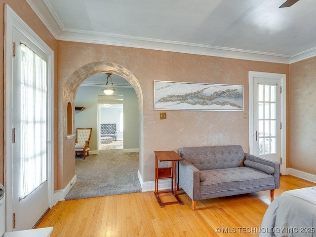 living area featuring arched walkways, light wood finished floors, crown molding, and baseboards