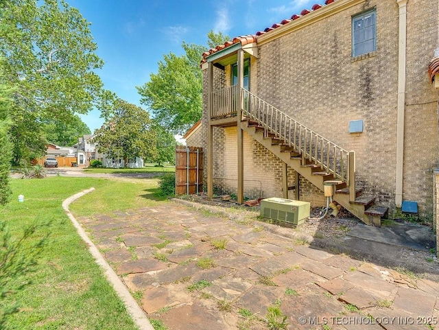 view of side of property with stairs, a patio, a tiled roof, a lawn, and stucco siding