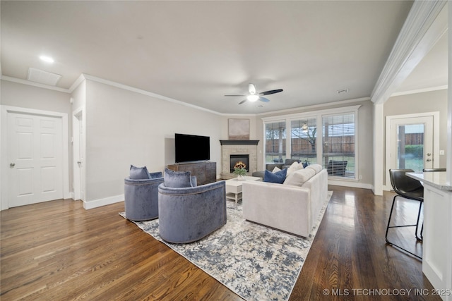 living room with a ceiling fan, dark wood-type flooring, baseboards, ornamental molding, and a stone fireplace