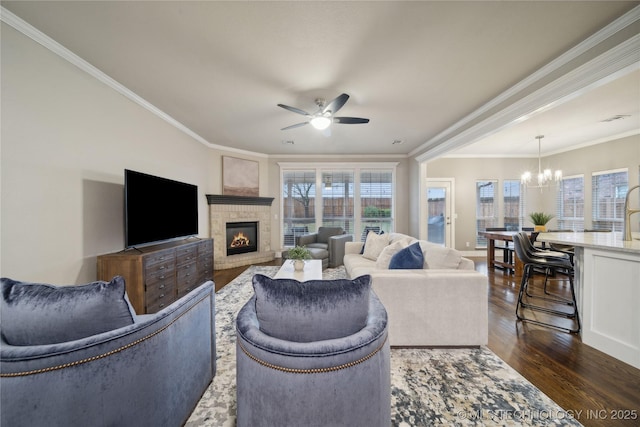 living room with a chandelier, dark wood finished floors, ceiling fan, a glass covered fireplace, and crown molding