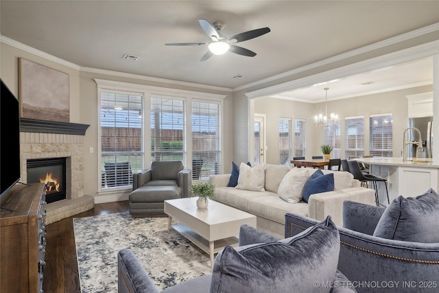 living room featuring wood finished floors, a chandelier, ceiling fan, a brick fireplace, and ornamental molding