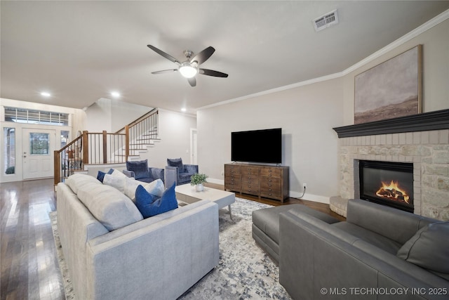 living area featuring stairway, a ceiling fan, crown molding, wood finished floors, and a fireplace