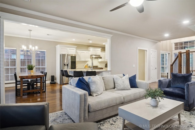 living area with a chandelier, ceiling fan, dark wood-style flooring, ornamental molding, and baseboards