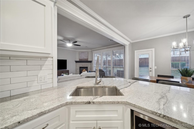 kitchen with ornamental molding, a sink, backsplash, a glass covered fireplace, and light stone counters