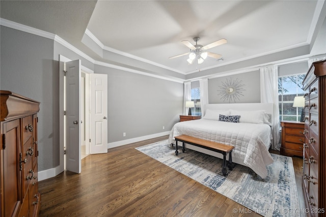bedroom with a tray ceiling, multiple windows, wood finished floors, ornamental molding, and baseboards