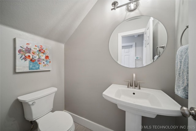half bathroom featuring toilet, a textured ceiling, baseboards, vaulted ceiling, and a sink