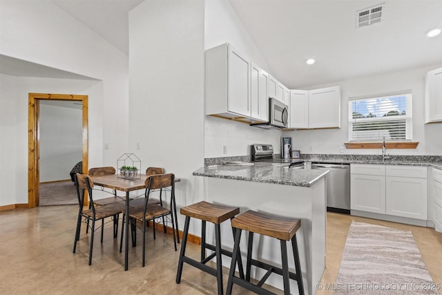 11879 Sandy Acres Trl, Kingston, OK 73439 - kitchen with stainless steel appliances, dark stone counters, white cabinets, concrete floors, and a breakfast bar