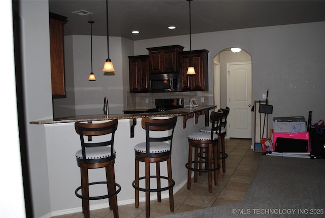 2025 E 134th St S, Bixby, OK 74008 - kitchen with stainless steel microwave, electric range oven, a breakfast bar area, arched walkways, and backsplash