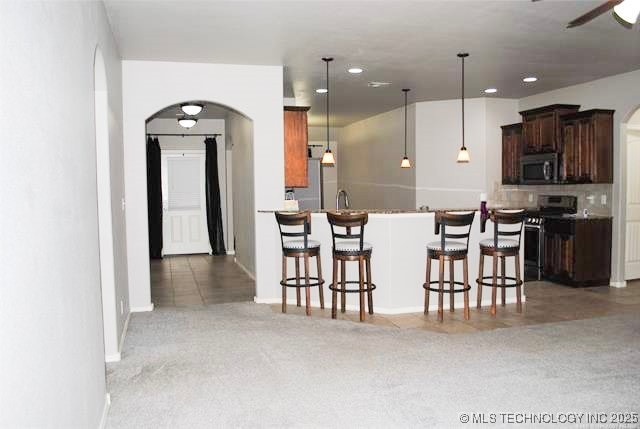 2025 E 134th St S, Bixby, OK 74008 - kitchen featuring appliances with stainless steel finishes, arched walkways, carpet, a kitchen breakfast bar, and decorative light fixtures