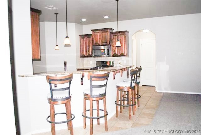 2025 E 134th St S, Bixby, OK 74008 - kitchen featuring stainless steel microwave, stove, arched walkways, a breakfast bar area, and decorative light fixtures