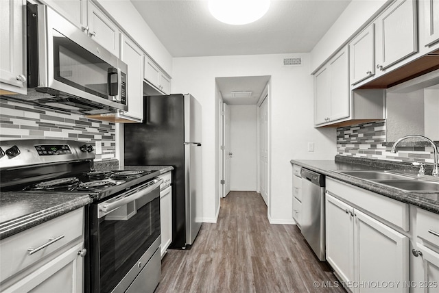 7911 E 66th St Unit 45H, Tulsa, OK 74133 - kitchen featuring appliances with stainless steel finishes, a sink, wood finished floors, dark countertops, and decorative backsplash