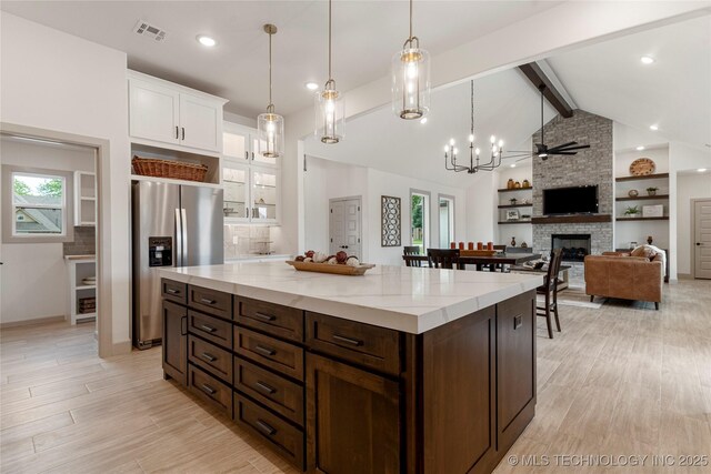 18258 S Clear Creek Ct, Claremore, OK 74017 - kitchen featuring stainless steel fridge, a fireplace, a chandelier, white cabinetry, and glass insert cabinets