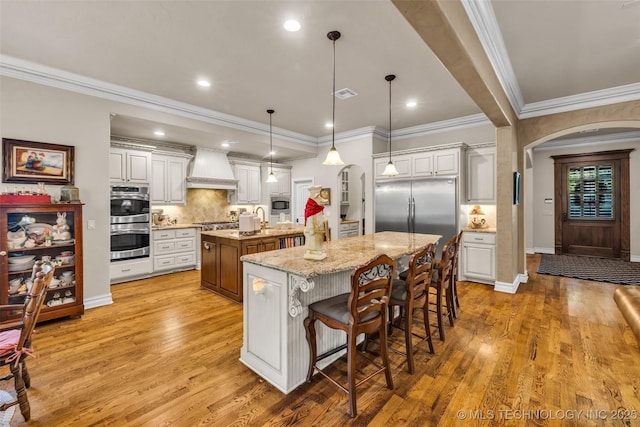 10942 S 93rd E Ave, Bixby, OK 74133 - kitchen featuring arched walkways, a large island, appliances with stainless steel finishes, custom exhaust hood, and crown molding