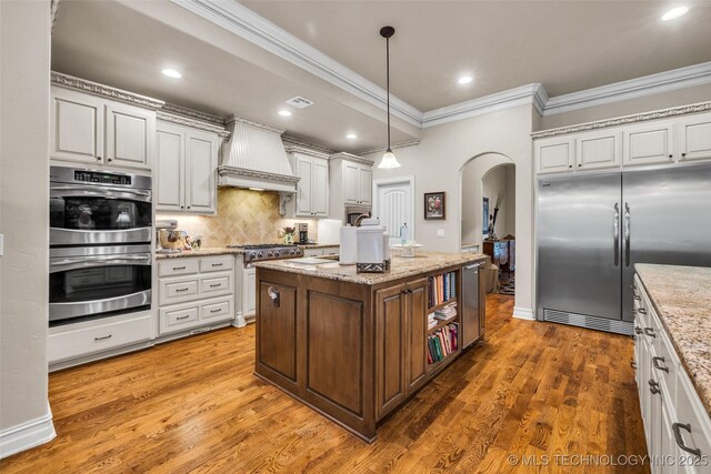 10942 S 93rd E Ave, Bixby, OK 74133 - kitchen featuring appliances with stainless steel finishes, arched walkways, premium range hood, ornamental molding, and tasteful backsplash