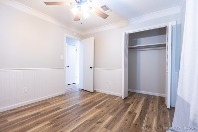 unfurnished bedroom featuring ornamental molding, wainscoting, wood finished floors, a closet, and a ceiling fan