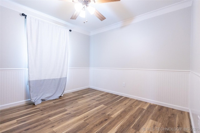 spare room with a wainscoted wall, wood finished floors, a ceiling fan, and ornamental molding