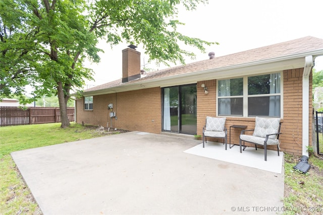 back of property with a chimney, brick siding, a patio, and a shingled roof