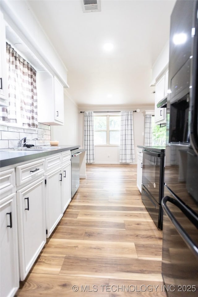 kitchen with white cabinets, dishwasher, light wood finished floors, backsplash, and ornamental molding