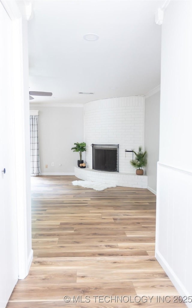 unfurnished living room with ornamental molding, light wood-style floors, a brick fireplace, ceiling fan, and baseboards