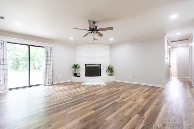 unfurnished living room with a ceiling fan, wood finished floors, ornamental molding, recessed lighting, and a brick fireplace