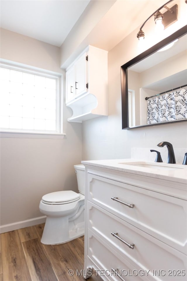 bathroom with toilet, vanity, wood finished floors, and baseboards