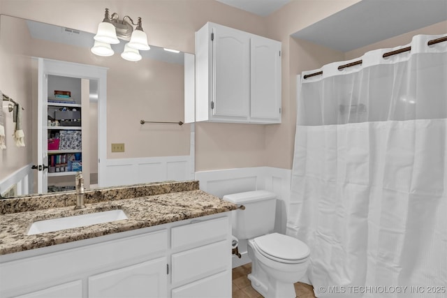bathroom with wainscoting, vanity, toilet, a decorative wall, and tile patterned floors