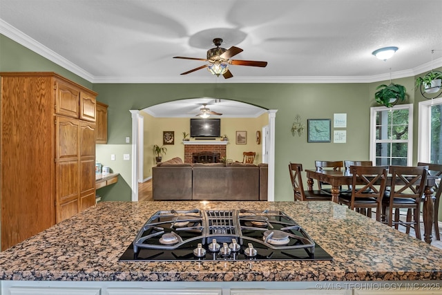 kitchen with ornate columns, ceiling fan, arched walkways, stovetop with downdraft, and a fireplace