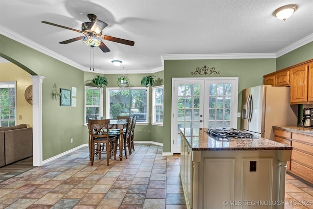kitchen featuring appliances with stainless steel finishes, a ceiling fan, arched walkways, french doors, and dark stone countertops