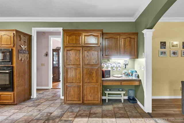 kitchen with black oven, built in microwave, baseboards, crown molding, and stone finish floors