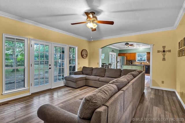 living area featuring a ceiling fan, arched walkways, healthy amount of natural light, a textured ceiling, and crown molding