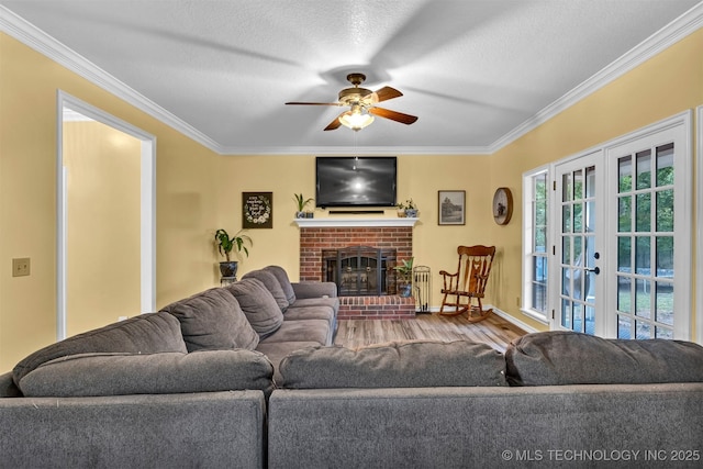 living room with crown molding, a ceiling fan, wood finished floors, french doors, and a fireplace