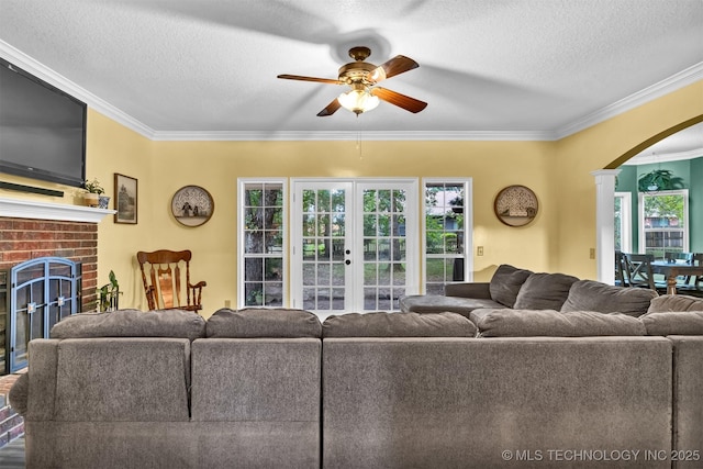 living area featuring a ceiling fan, ornamental molding, arched walkways, a brick fireplace, and a textured ceiling