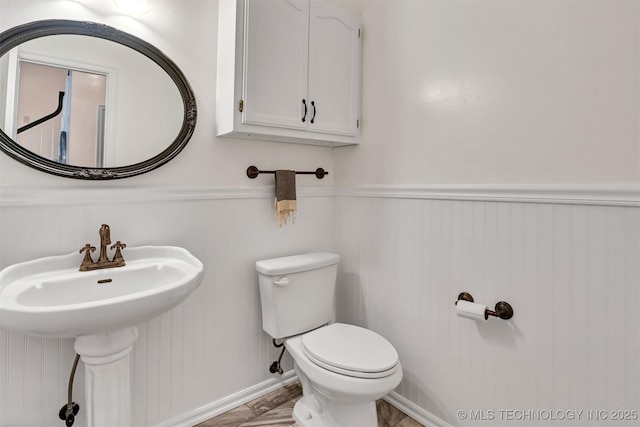 half bath featuring toilet, a wainscoted wall, and a sink