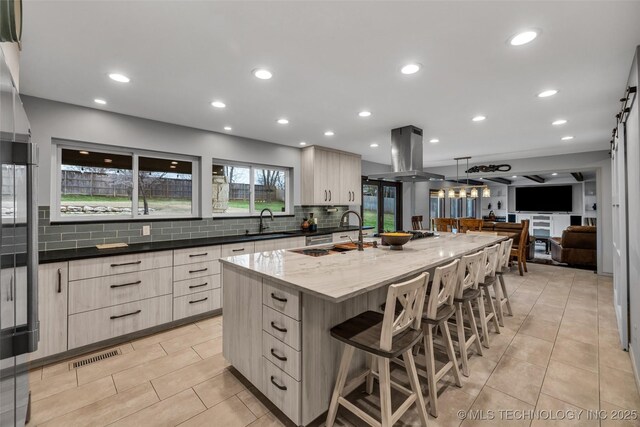 9417 S Gary Ave, Tulsa, OK 74137 - kitchen featuring island range hood, backsplash, a large island with sink, a breakfast bar area, and light tile patterned floors