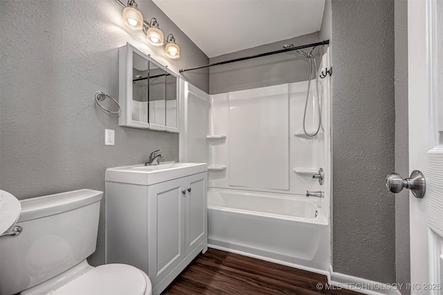 423 E Cherry St, Cushing, OK 74023 - bathroom featuring a textured wall, wood finished floors, toilet, vanity, and washtub / shower combination