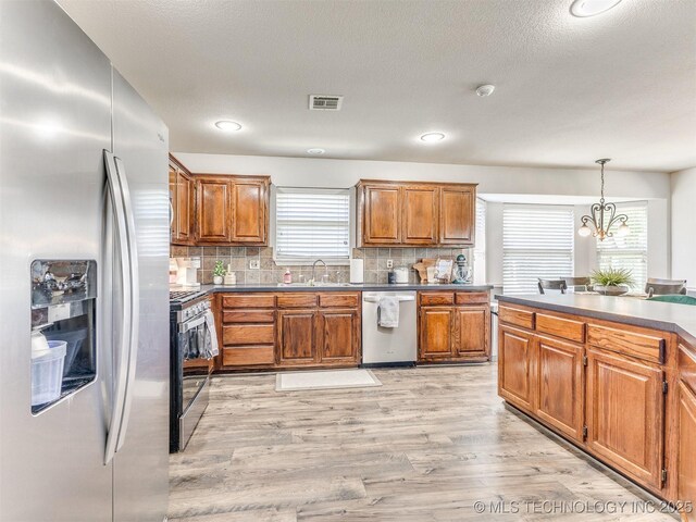 2008 N 8th St, Broken Arrow, OK 74012 - kitchen with stainless steel appliances, a sink, brown cabinets, light wood-style floors, and a textured ceiling