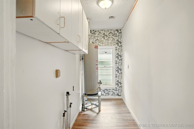 850 E Moses St, Cushing, OK 74023 - corridor with wallpapered walls, light wood finished floors, baseboards, a textured ceiling, and water heater