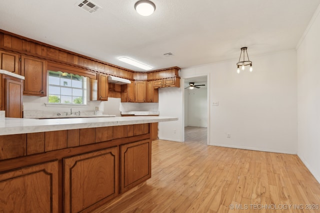9590 S 4240th Rd, Chelsea, OK 74016 - kitchen featuring brown cabinetry, light countertops, light wood-type flooring, baseboards, and decorative light fixtures
