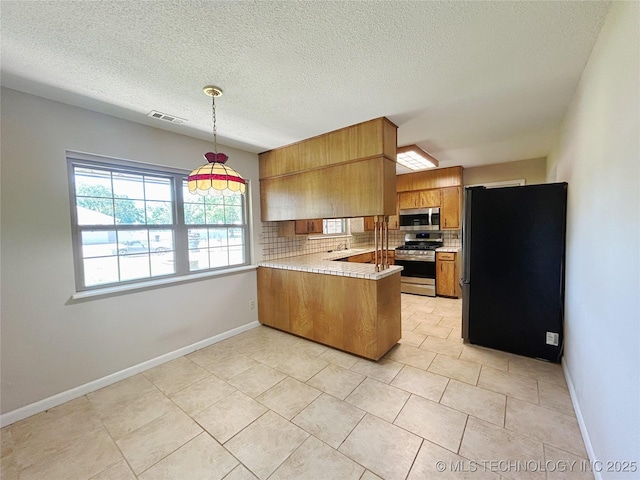 502 W Elm St, Henryetta, OK 74437 - kitchen with stainless steel appliances, brown cabinets, a peninsula, light countertops, and tasteful backsplash