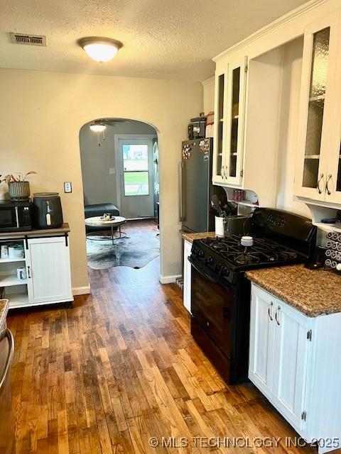2201 Baugh St, Muskogee, OK 74403 - kitchen featuring black appliances, arched walkways, white cabinetry, dark wood-style flooring, and a textured ceiling