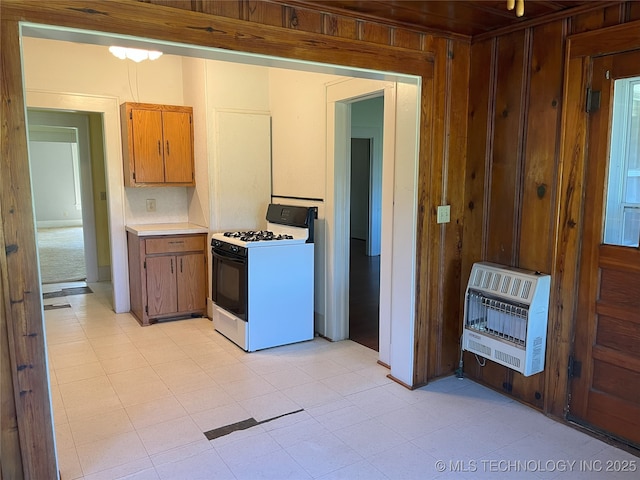 701 NW 3rd St, Stigler, OK 74462 - kitchen with range with gas stovetop, heating unit, light countertops, wooden walls, and brown cabinets