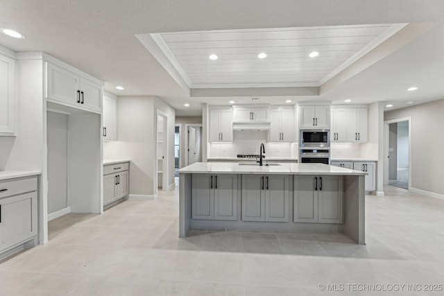 23250 E 106th Pl S, Broken Arrow, OK 74014 - kitchen with appliances with stainless steel finishes, a tray ceiling, baseboards, under cabinet range hood, and light countertops