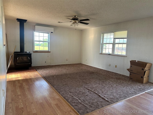 621 S 3rd St, Morris, OK 74445 - unfurnished living room with a wall mounted AC, a wood stove, wood finished floors, a textured ceiling, and ceiling fan
