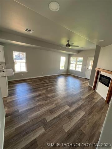 130 W Lincoln Ave, Sapulpa, OK 74066 - unfurnished living room featuring ceiling fan, a glass covered fireplace, dark wood-type flooring, and plenty of natural light