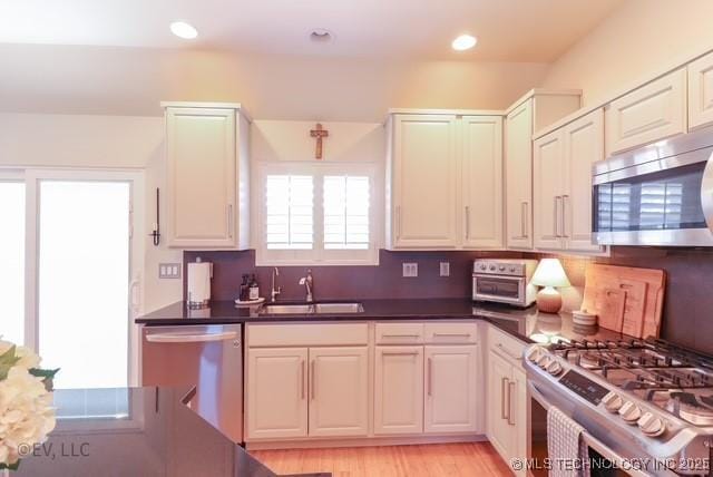 14538 S Kendalwood Blvd E, Glenpool, OK 74033 - kitchen with appliances with stainless steel finishes, a sink, dark countertops, decorative backsplash, and light wood-style flooring