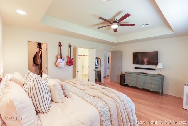 14538 S Kendalwood Blvd E, Glenpool, OK 74033 - bedroom featuring a raised ceiling, light wood-type flooring, a spacious closet, ensuite bath, and a ceiling fan