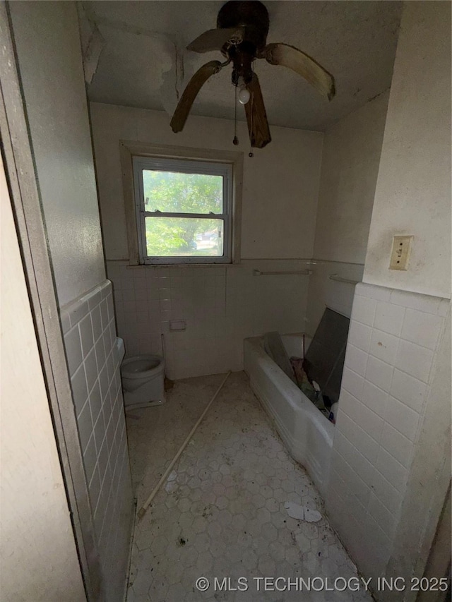 710 F St NW, Ardmore, OK 73401 - bathroom featuring tile walls, toilet, a bathtub, a ceiling fan, and a wainscoted wall