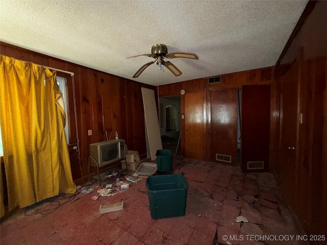 710 F St NW, Ardmore, OK 73401 - unfurnished living room with ceiling fan, a textured ceiling, arched walkways, and wooden walls