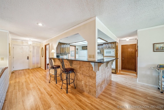 13200 E 130th St S, Broken Arrow, OK 74011 - kitchen featuring white appliances, a breakfast bar area, light wood-type flooring, dark countertops, and a textured ceiling