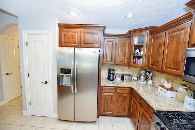 2570 Ambers Way, Tahlequah, OK 74464 - kitchen featuring appliances with stainless steel finishes, light tile patterned floors, tasteful backsplash, light stone countertops, and a textured ceiling